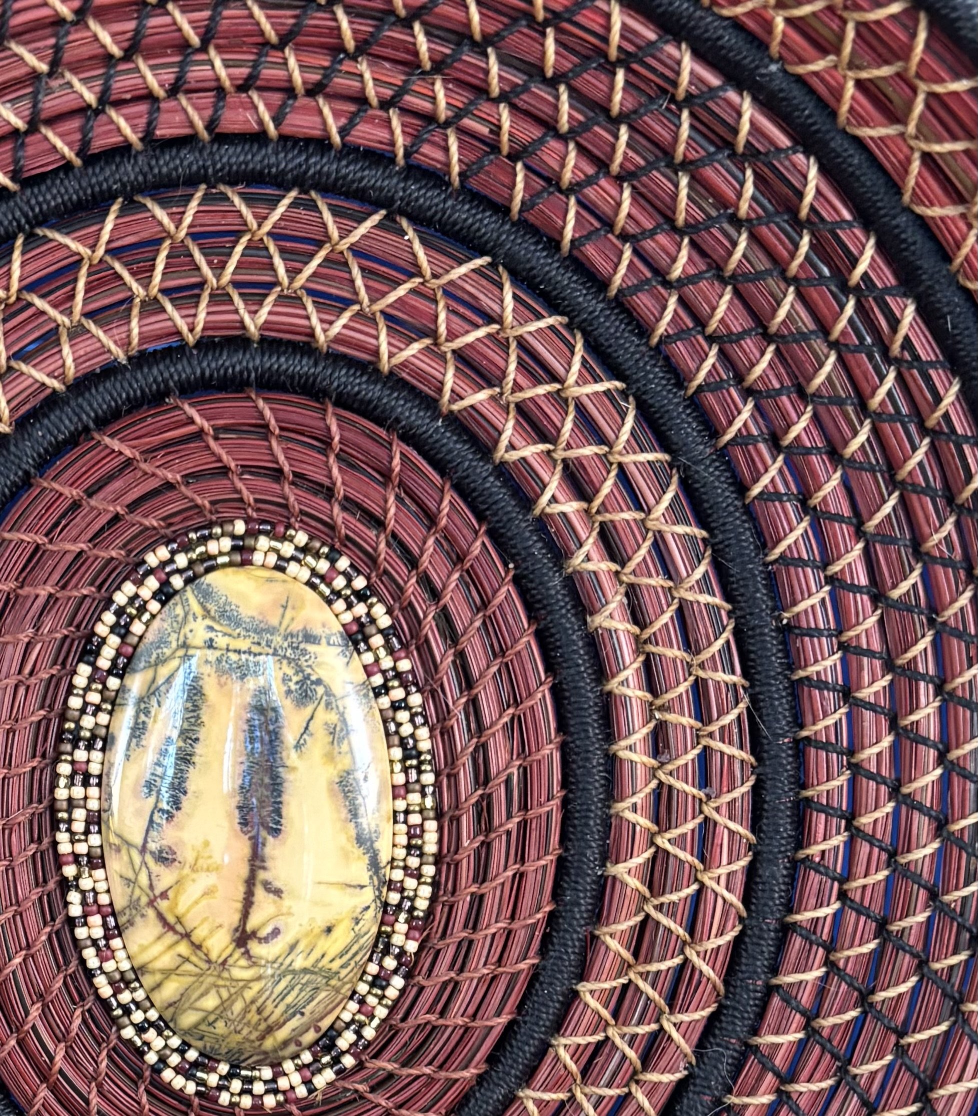 Detail of diamond stitching on red-dyed pine needle basket with black and caramel thread