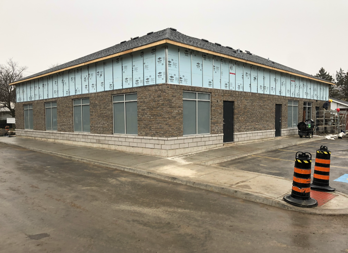 Building under construction with brick walls, large windows, a new roof, and construction materials and equipment nearby.
