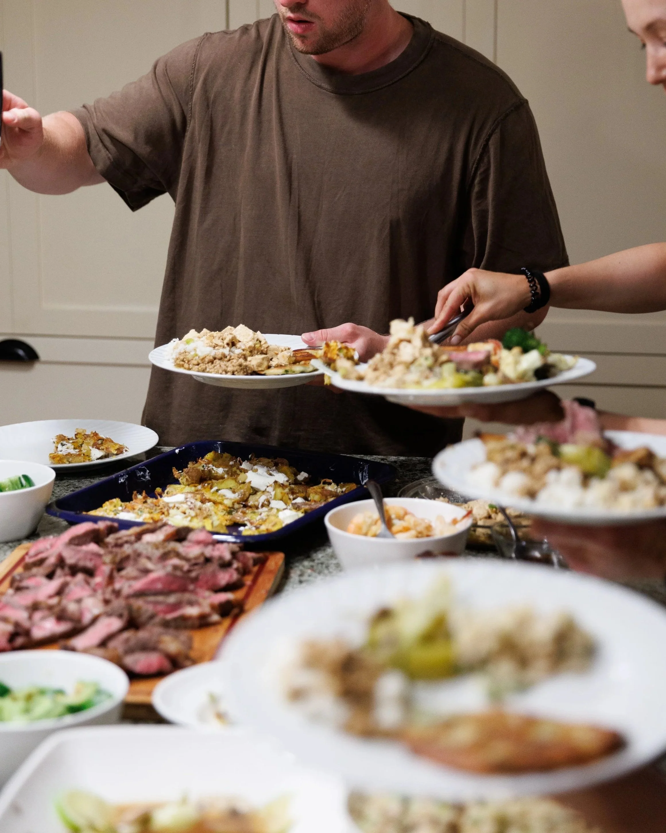 People serving and preparing various dishes at a buffet table, including bowls and trays of food.