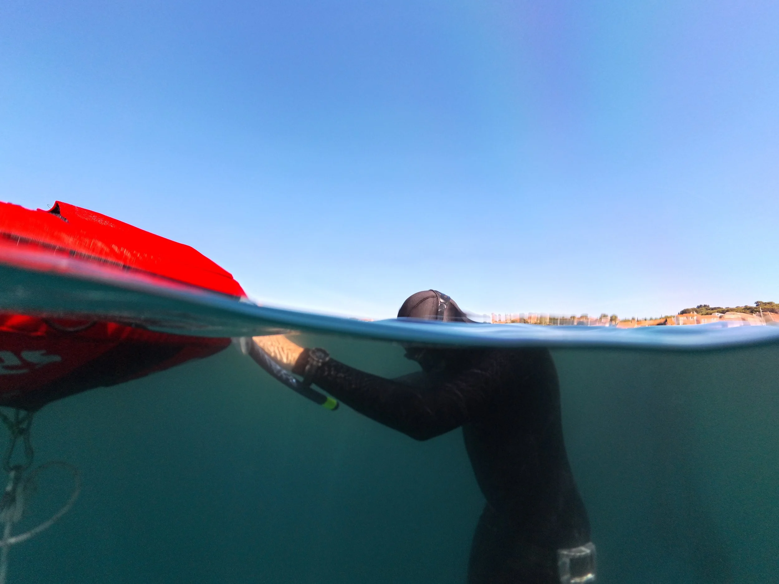 Photo sous-marine, montrant un paysage marin avec une partie d'une bouée d'entrainement, le ciel bleu et un horizon lointain.