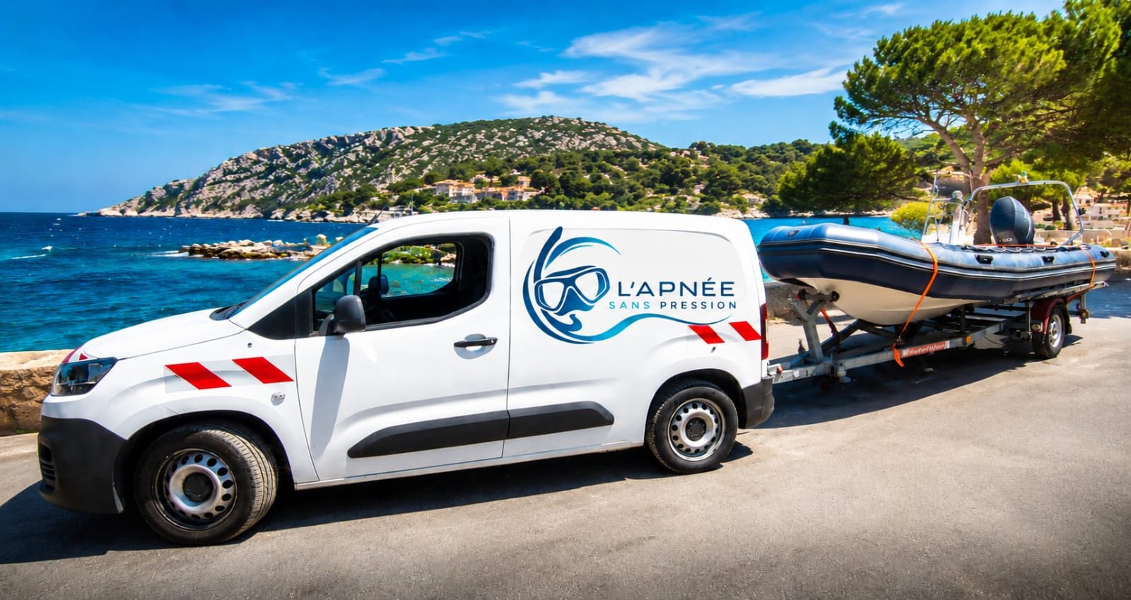 Une camionnette blanche avec un bateau hors bord sur remorque, stationnée près de la mer avec une montagne en arrière-plan.
