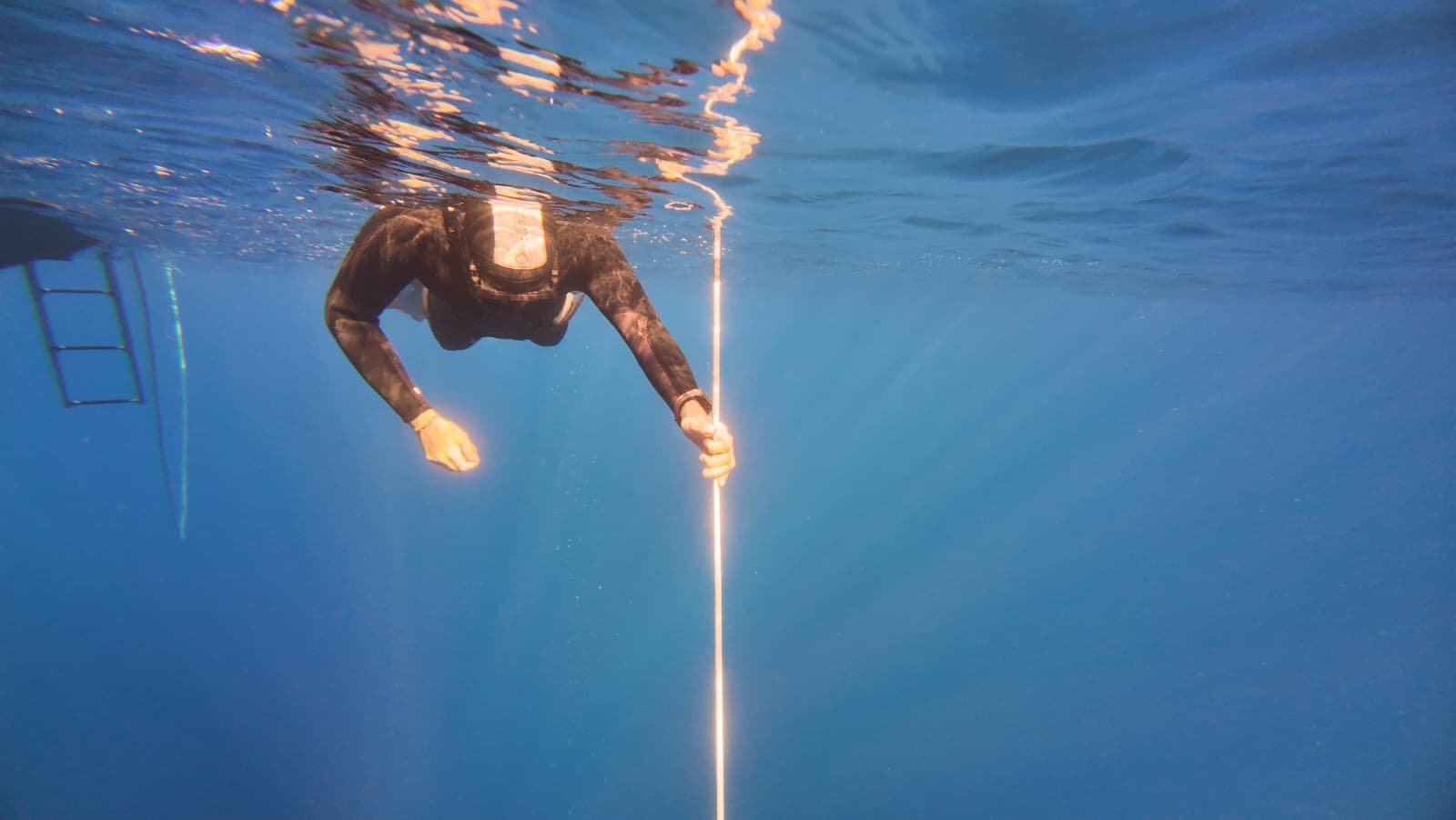 Personne en combinaison de plongée utilisant un instrument de mesure sous l'eau, avec une plateforme d'accès visible à gauche.