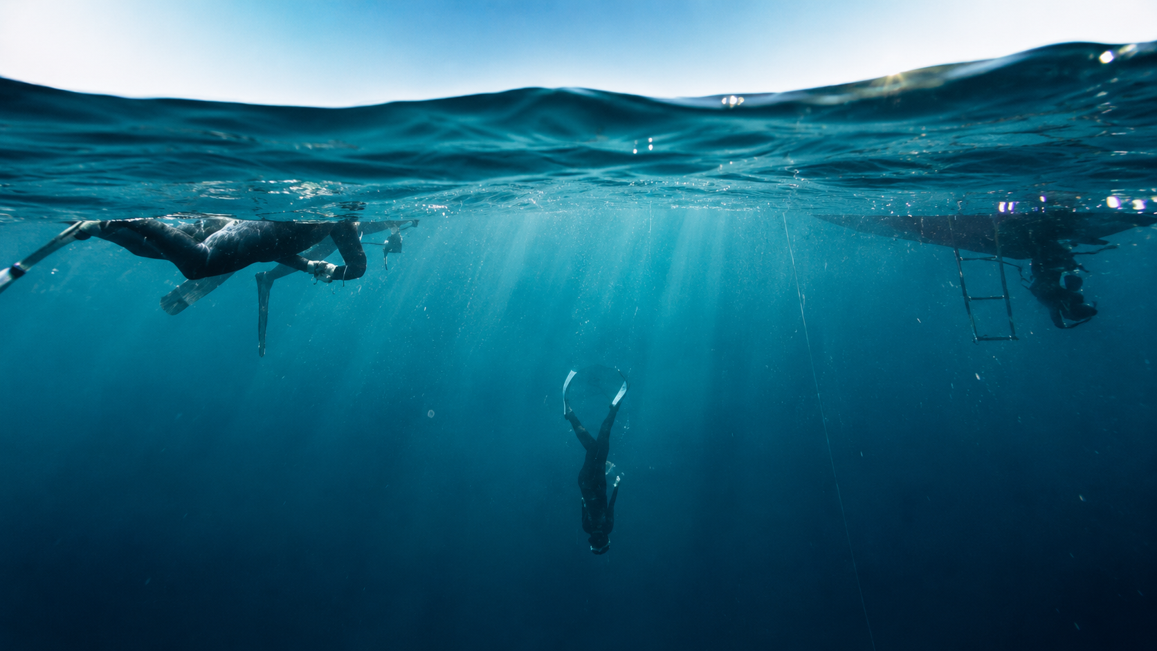 Scène sous-marine avec deux plongeurs, un avec une voiture sous l'eau, un avec une échelle, lumière solaire filtrant l'eau.