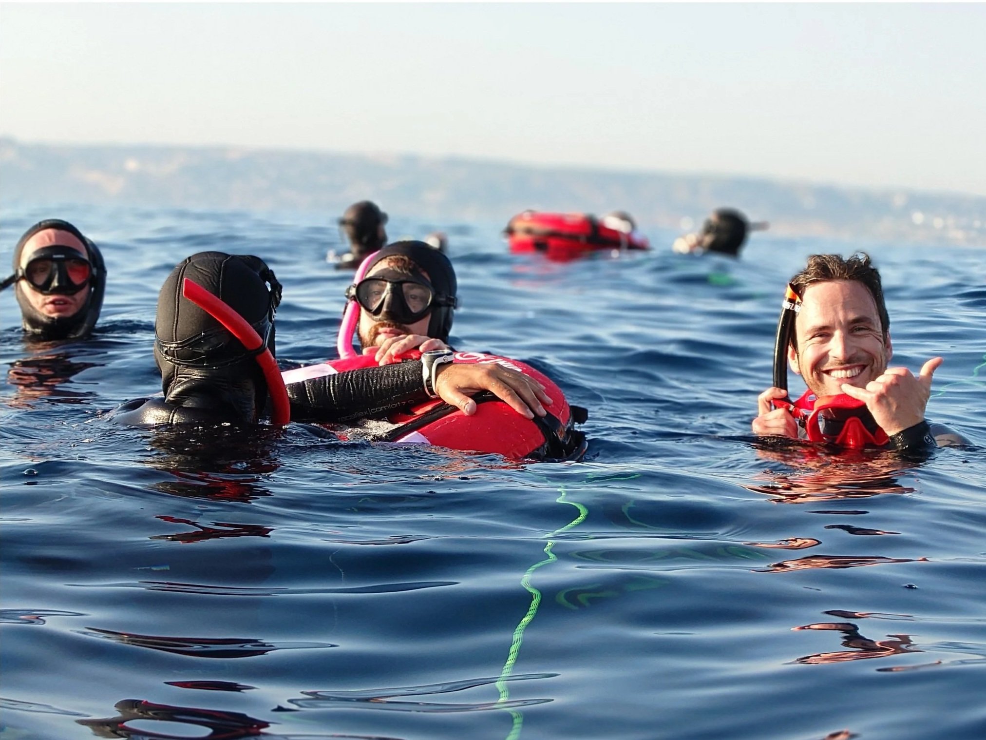 Groupe de personnes en plongée sous-marine dans la mer avec équipements de plongée, certains sourient et montrent la main en signe de succès.