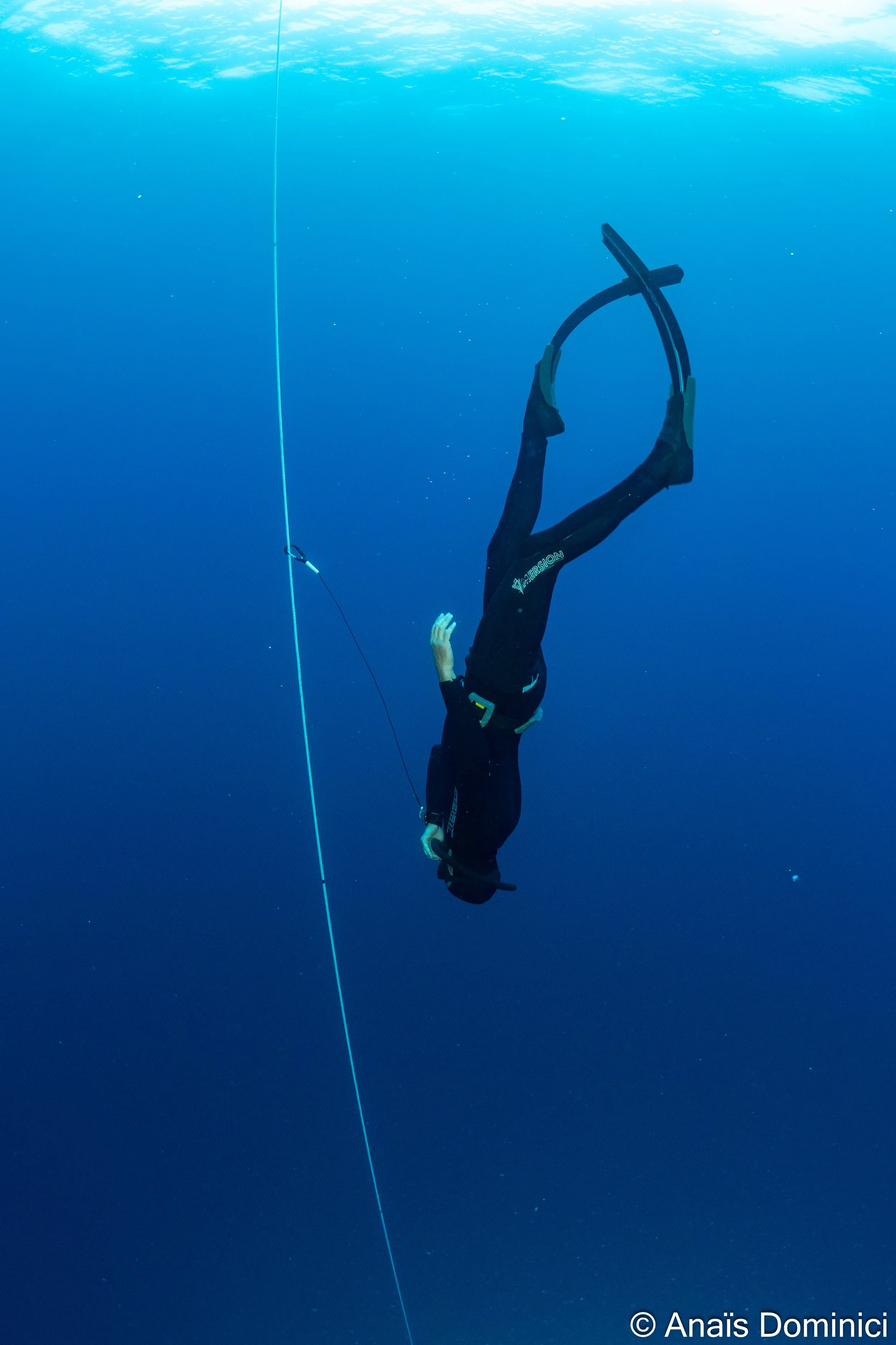 Une personne en combinaison de plongée nage sous l'eau, attachée à une ligne de sécurité bleue.