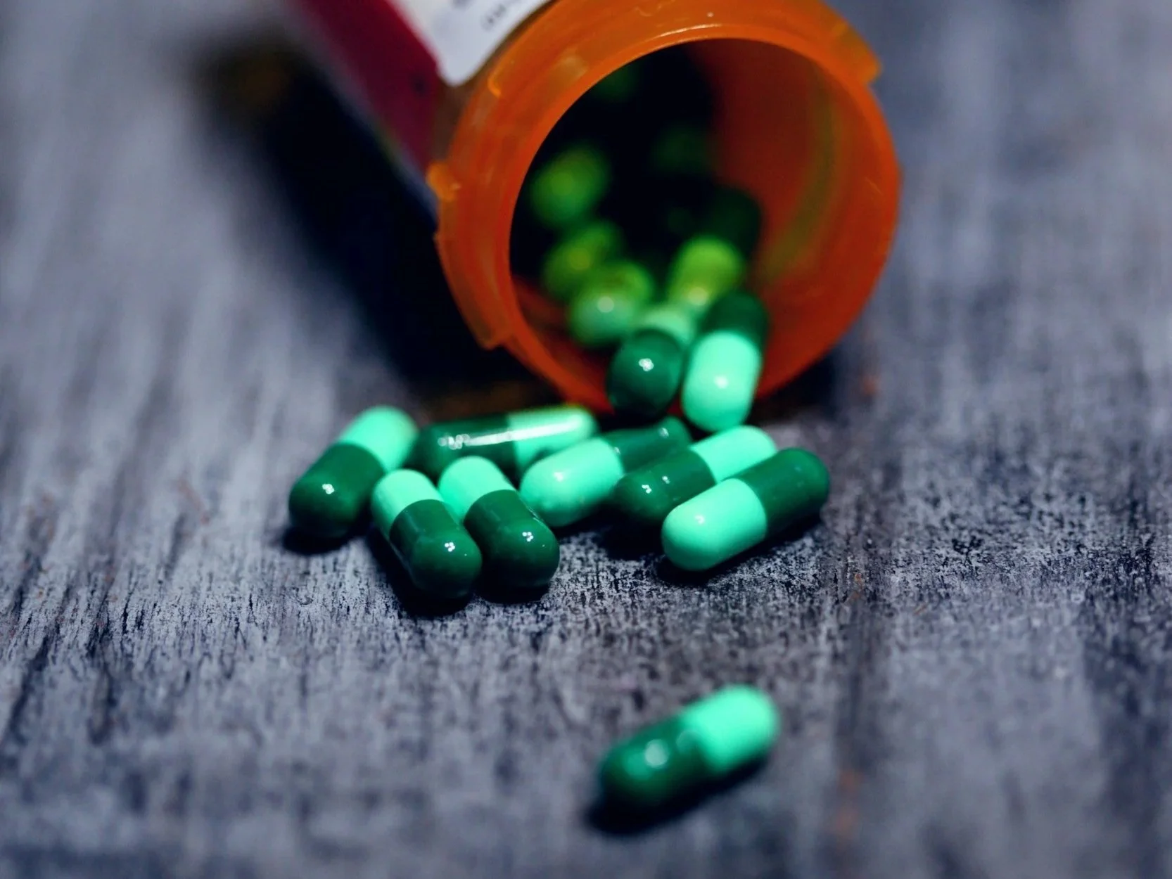 Green capsules spilling out of an orange pill bottle onto a wooden surface.