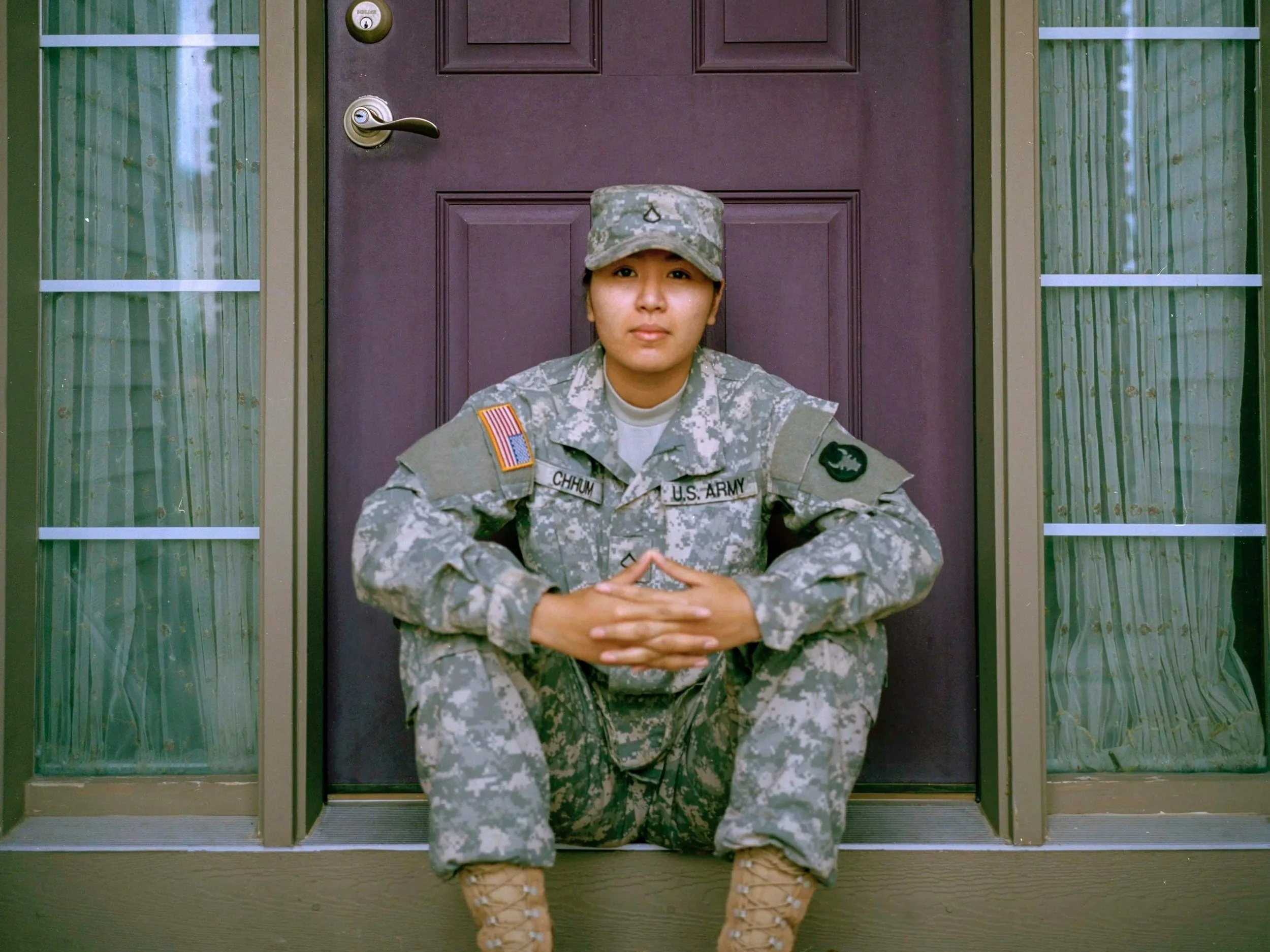 A woman in military uniform sitting on a step in front of a door with glass side panels.