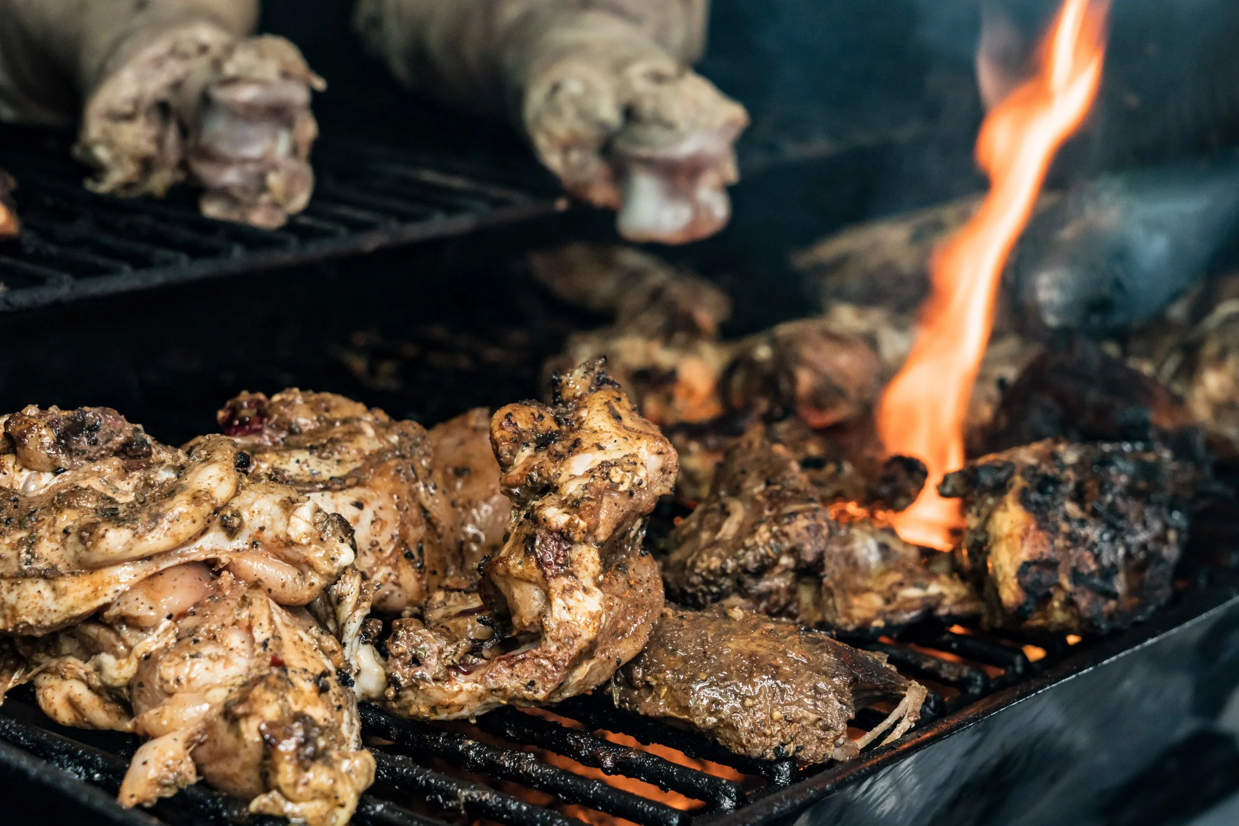 Meat and chicken pieces grilling on a BBQ with visible flames.