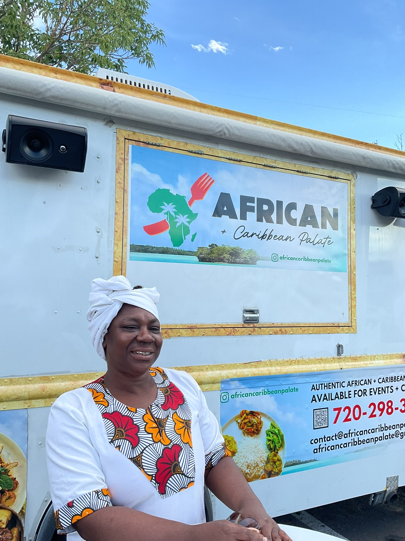 A woman wearing a white head wrap and colorful African pattern dress standing in front of a food truck with Africa's map outline, palm trees, and water, promoting African and Caribbean cuisine.