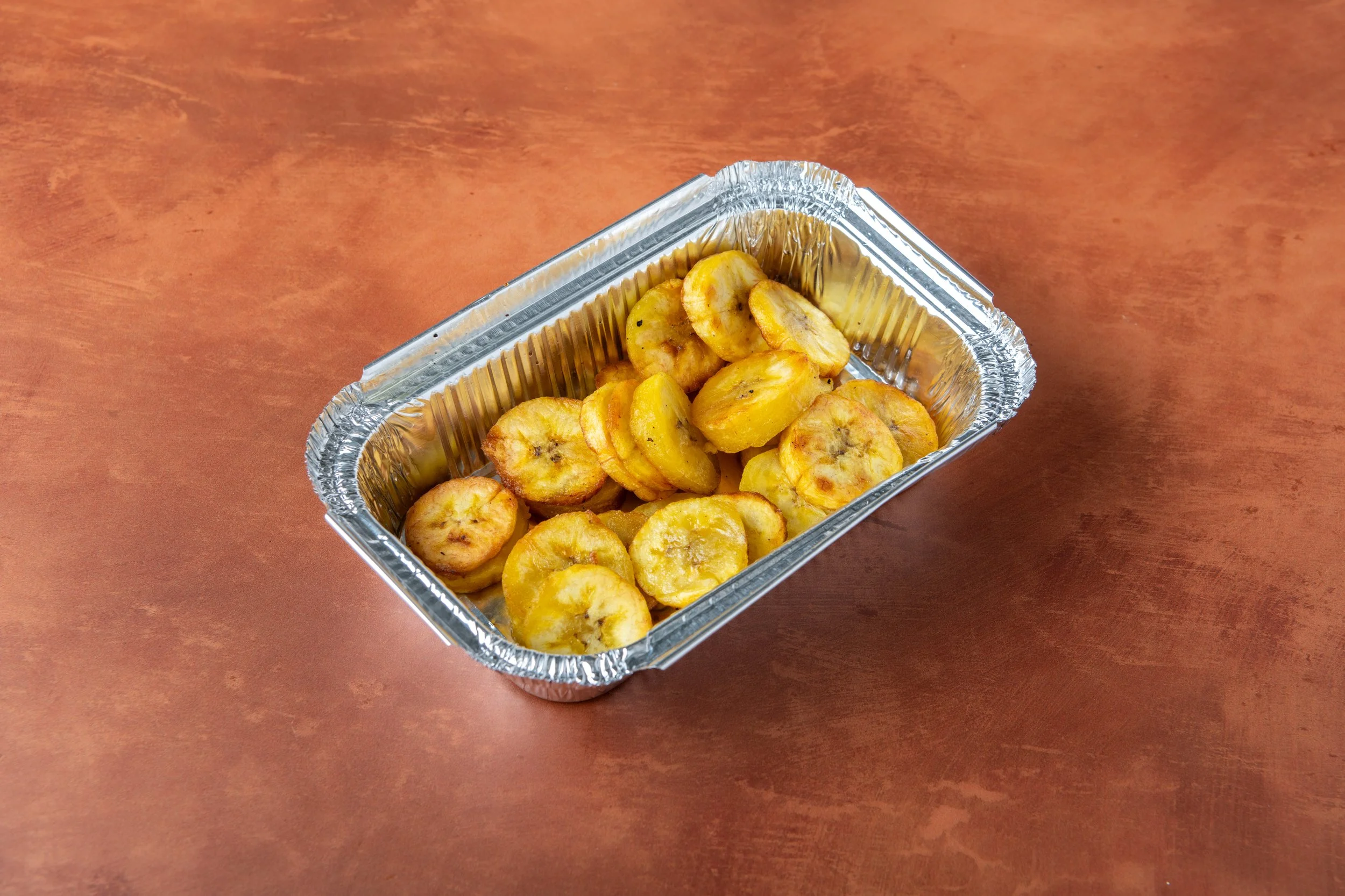 Small aluminum tray filled with fried plantain slices on a wooden table.