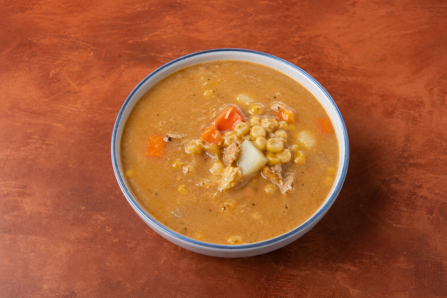 Close-up of a bowl of creamy vegetable soup with corn, carrots, and potatoes on a wooden surface.