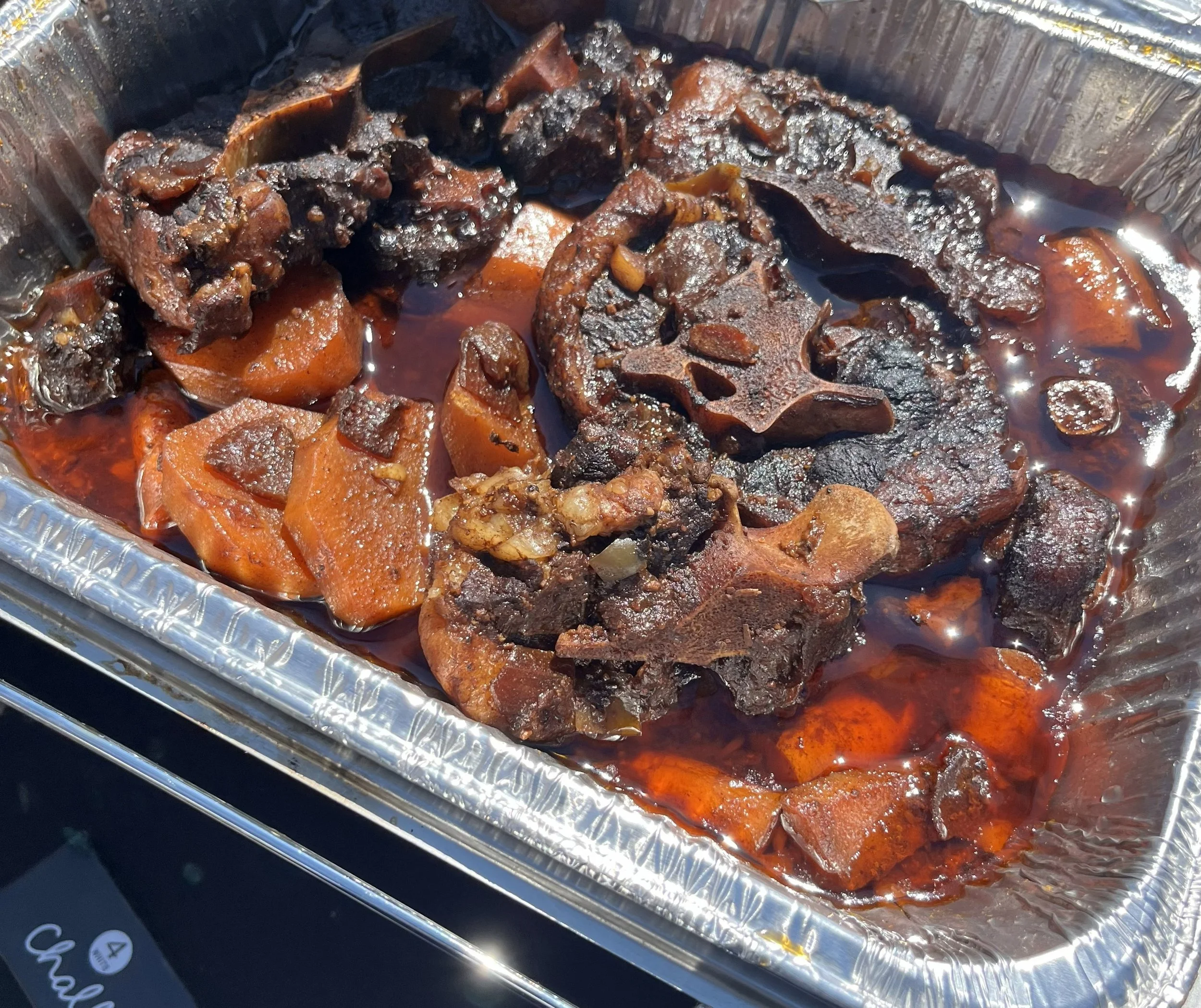 Barbecue ribs with a dark, sticky glaze, served in a disposable aluminum tray.