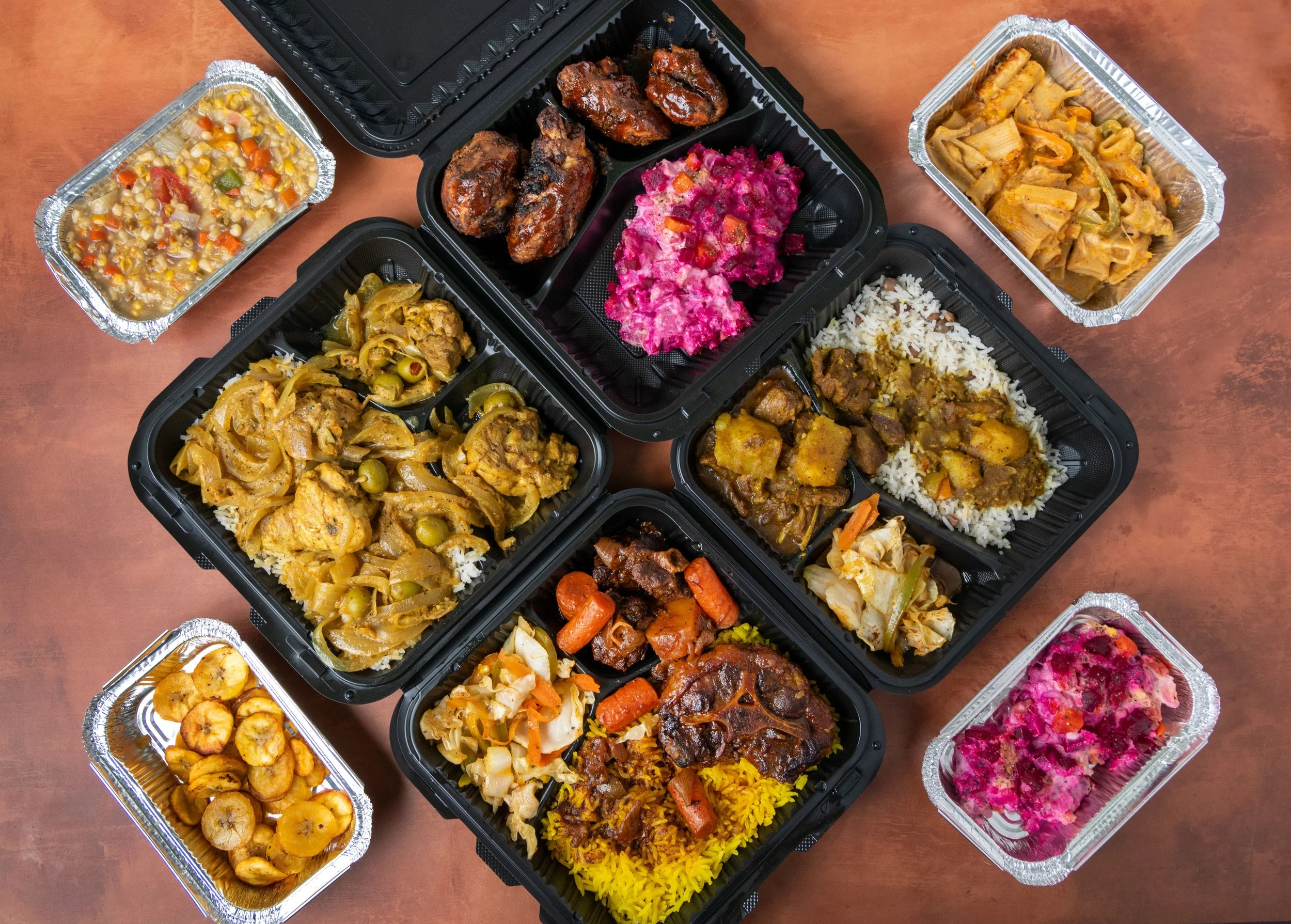 A variety of takeaway dishes displayed in black plastic containers and aluminum foil trays, including rice, meat stews, vegetables, salads, and desserts, set on a wooden surface.