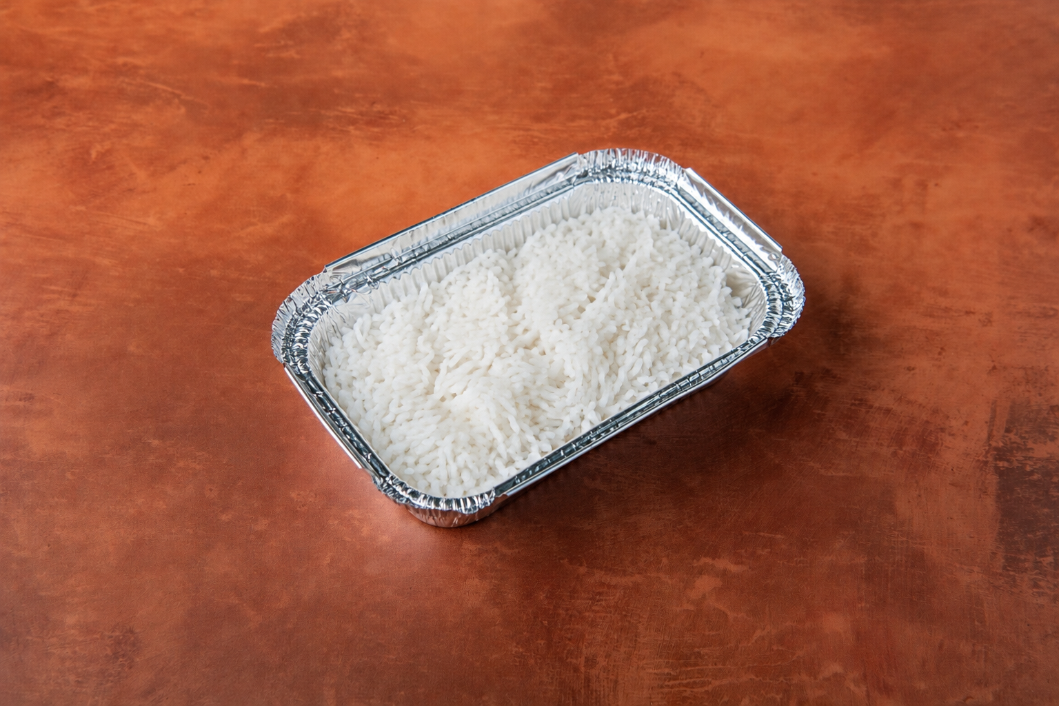 Aluminum tray filled with cooked white rice on a wooden surface.