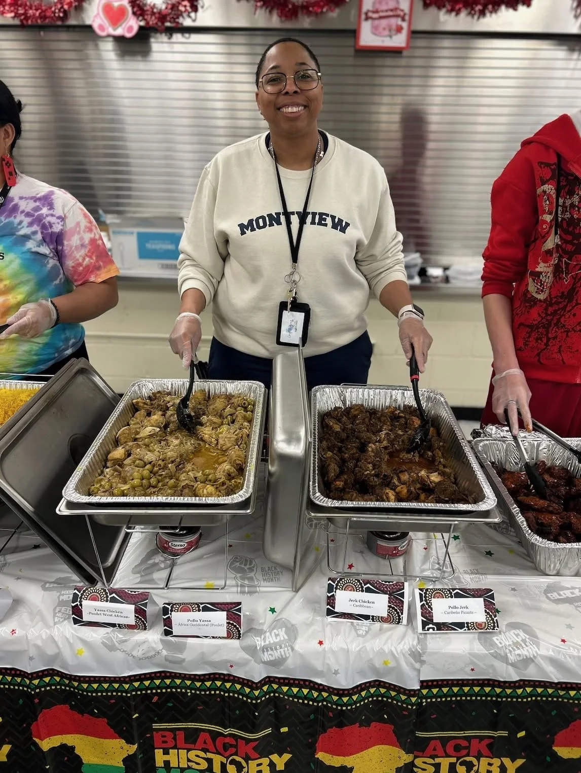 Woman smiling at food stall with two trays of cooked meat, one chicken and one beef, at a Black History Month event.