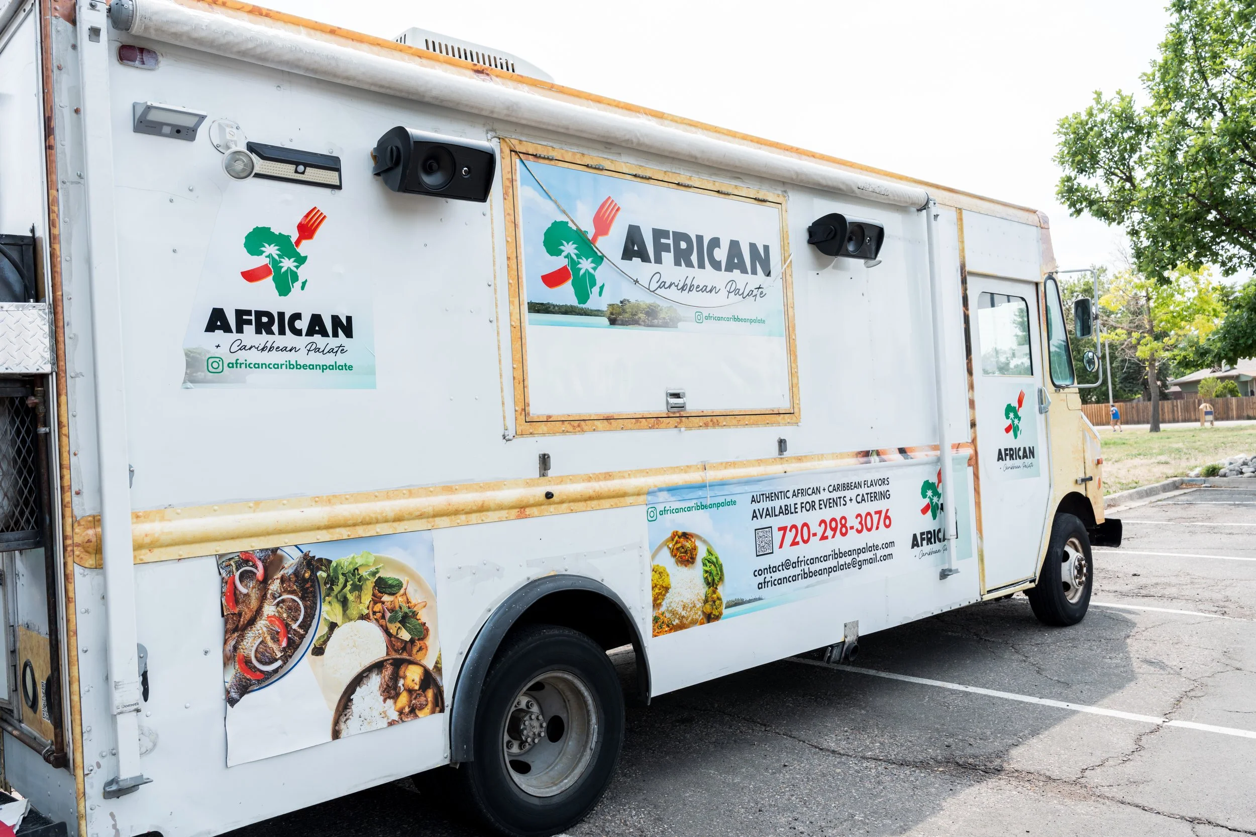 Food truck with African Caribbean Palate branding, featuring images of dishes and a map of Africa with a fork, parked in a parking lot with trees in the background.