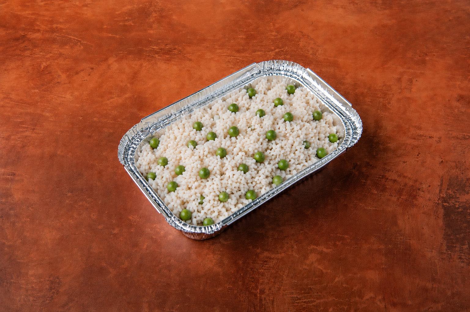Tray of white rice with green peas on a wooden surface.