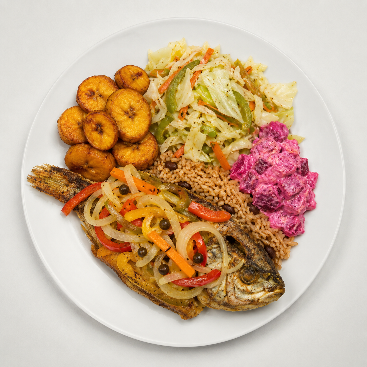 Plate of food with fried plantains, grilled fish topped with sautéed vegetables, rice and beans, mixed vegetables, and beet potato salad with pink dressing.