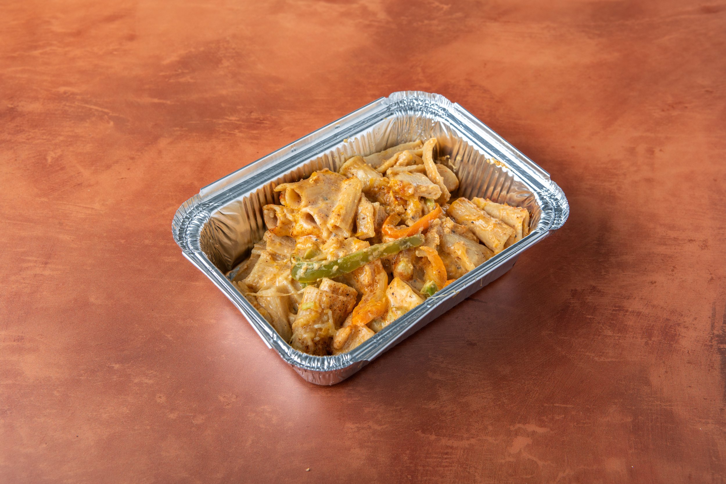 Takeout container with creamy pasta and vegetables on a wooden surface.