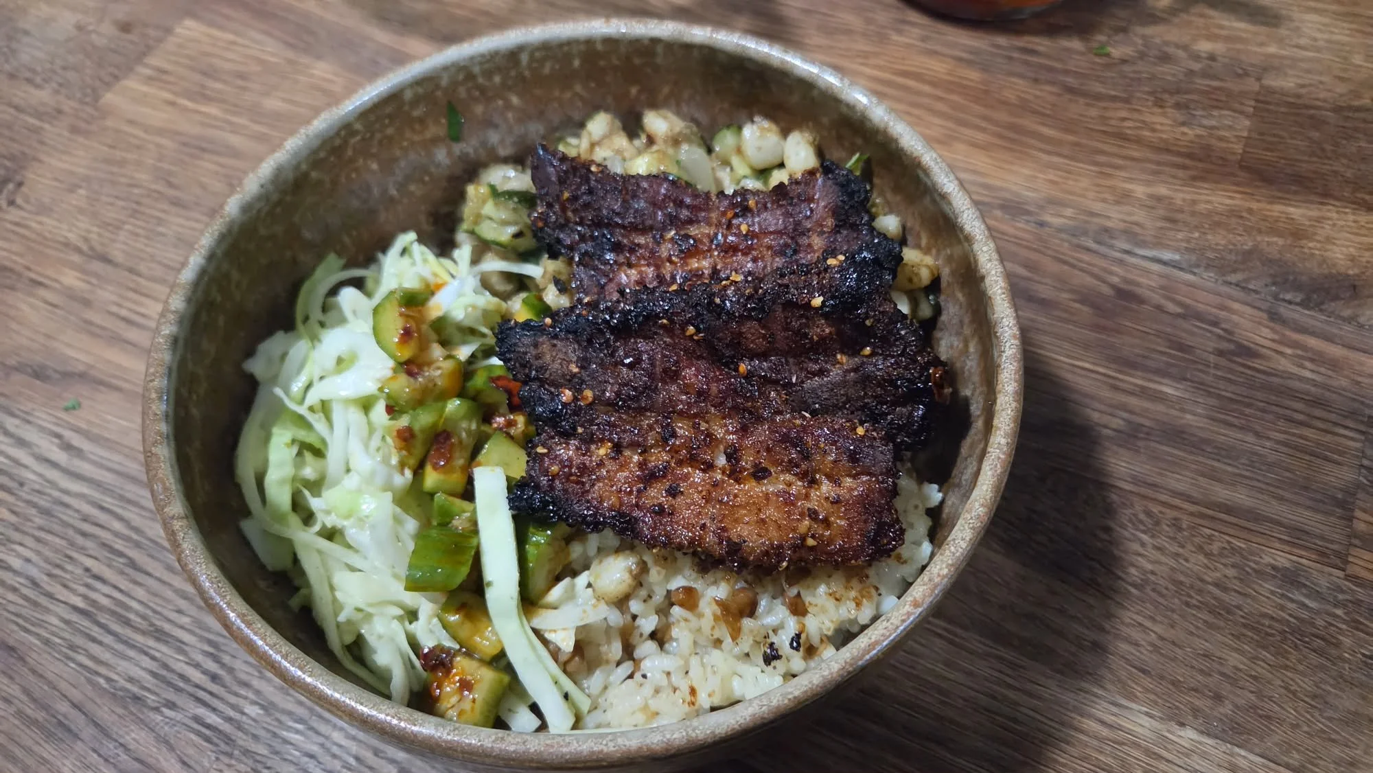 Bowl of lentils and rice topped with caramelized pork belly and a lime and cilantro cabbage slaw with sesame chili smashed cucumbers.