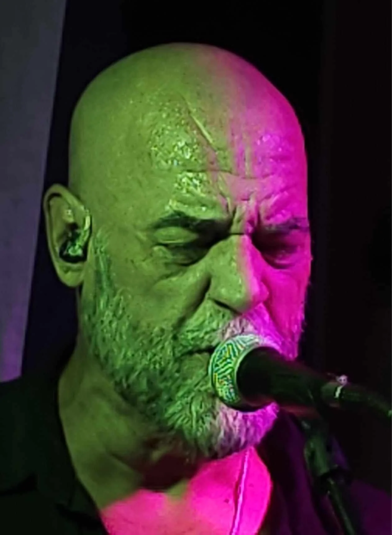 Larry Holly singing with his current short beard under green and magenta stage lighting