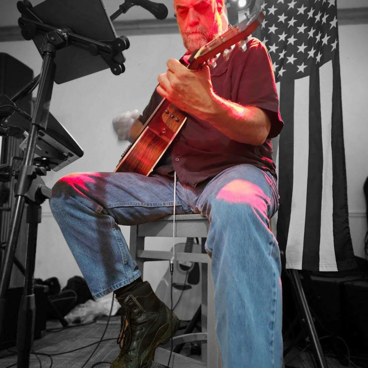 Low-angle view of Larry Holly playing acoustic guitar beneath dramatic red stage light