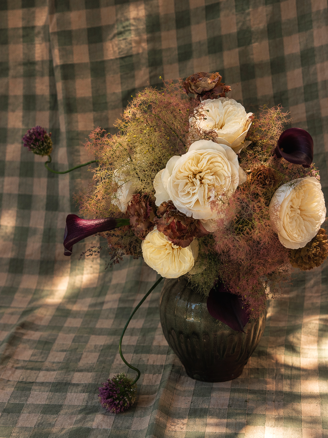 Sculptural white and burgundy floral arrangement with calla lilies and textural greenery by The Burrow.