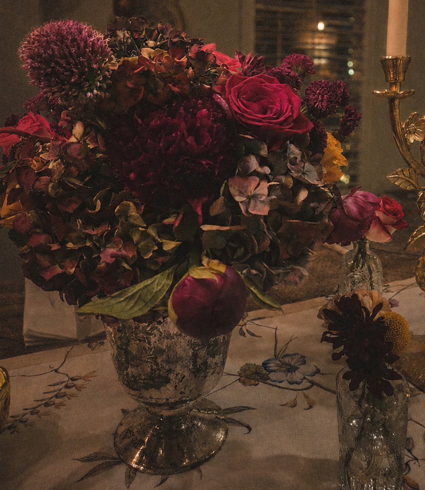 Moody red and burgundy floral arrangement with roses, dark foliage, and dramatic textural elements.