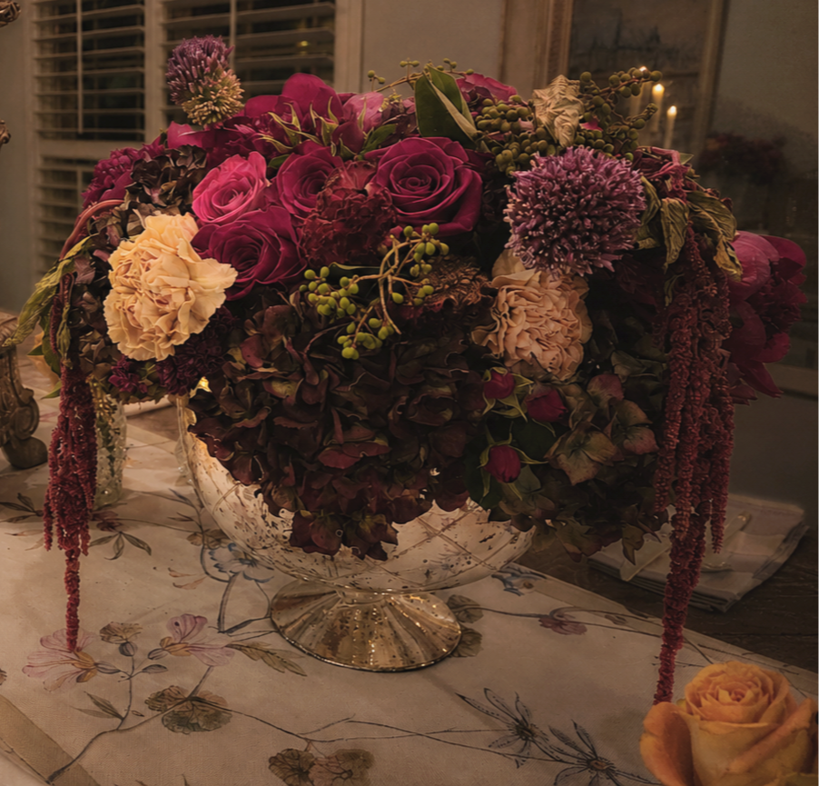 Artistic pink and burgundy floral arrangement with layered blooms, greenery, and organic movement.