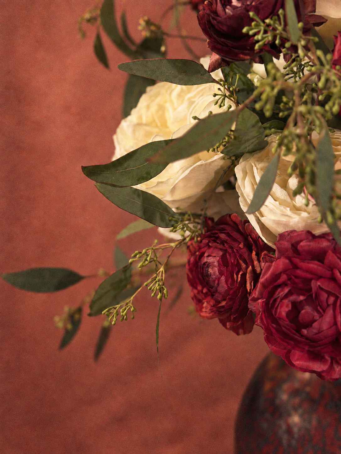 Close-up of a bouquet of flowers with red and white roses and green leaves in a vase on a wooden surface.