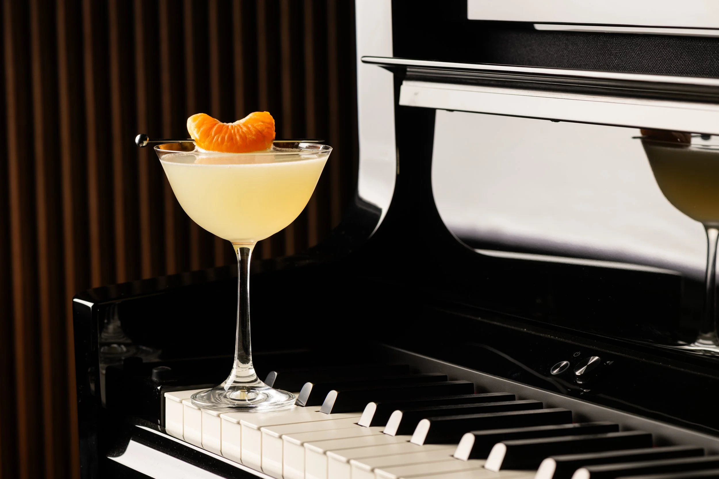 A cocktail glass with a bright orange garnish resting on the rim, placed on a piano keyboard.