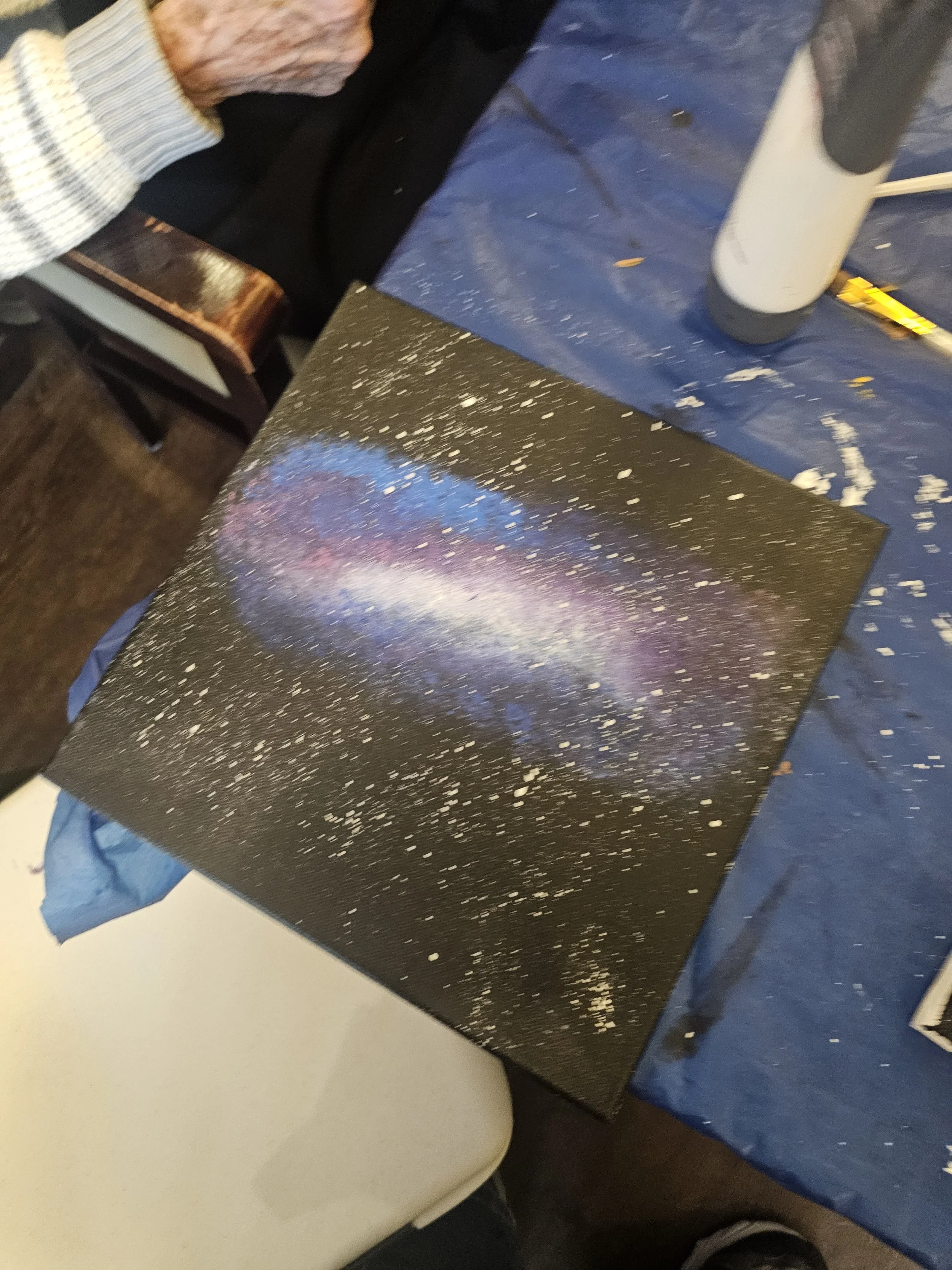Close-up of a freshly painted, black table with a galaxy design, including colorful swirls of pink, purple, and blue, and white speckles resembling stars.