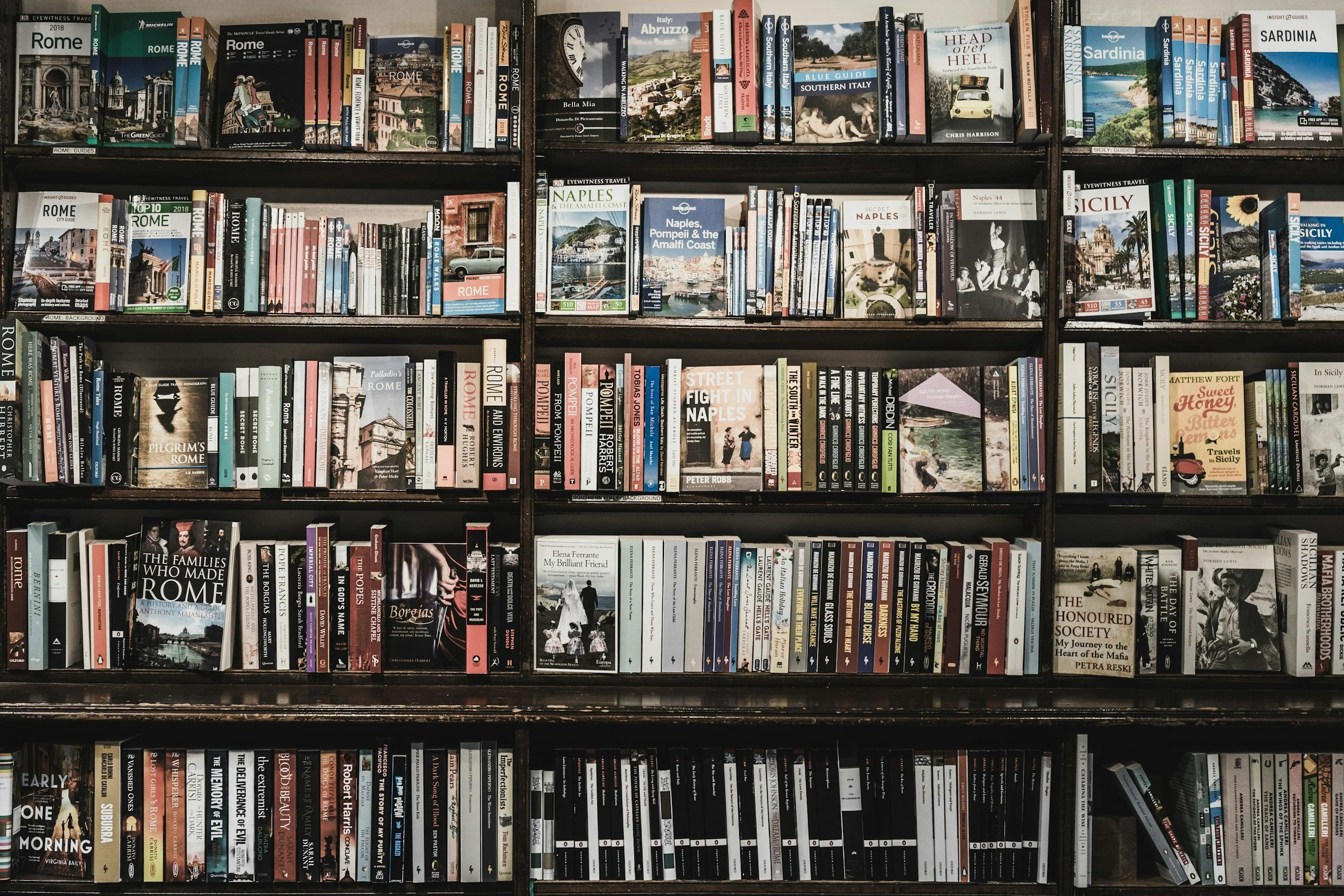 Shelf filled with travel guidebooks about Rome and Sicily, including titles on history, travel tips, and maps.