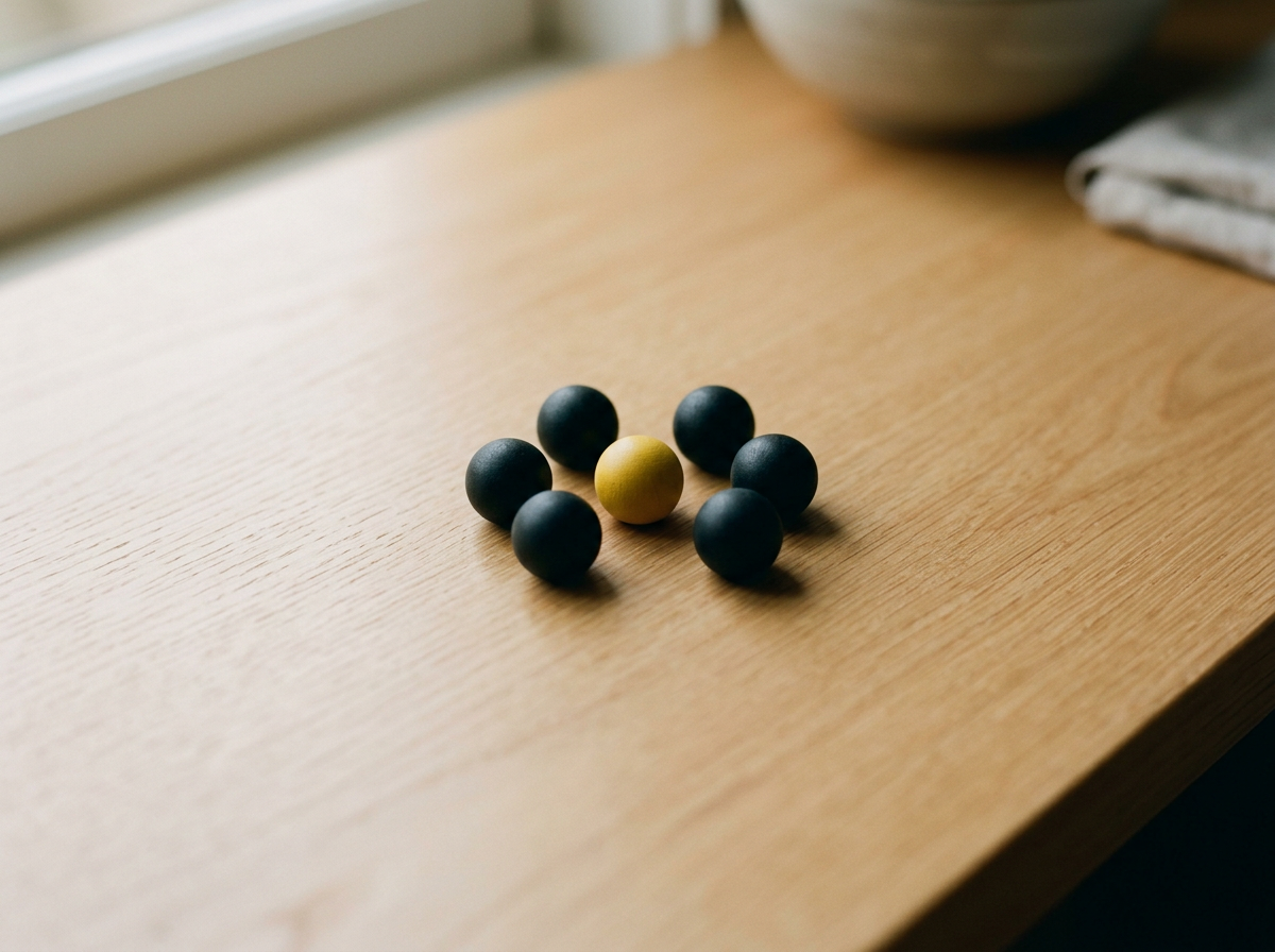 Seven black balls and one yellow ball arranged in a circle on a wooden surface near a window.