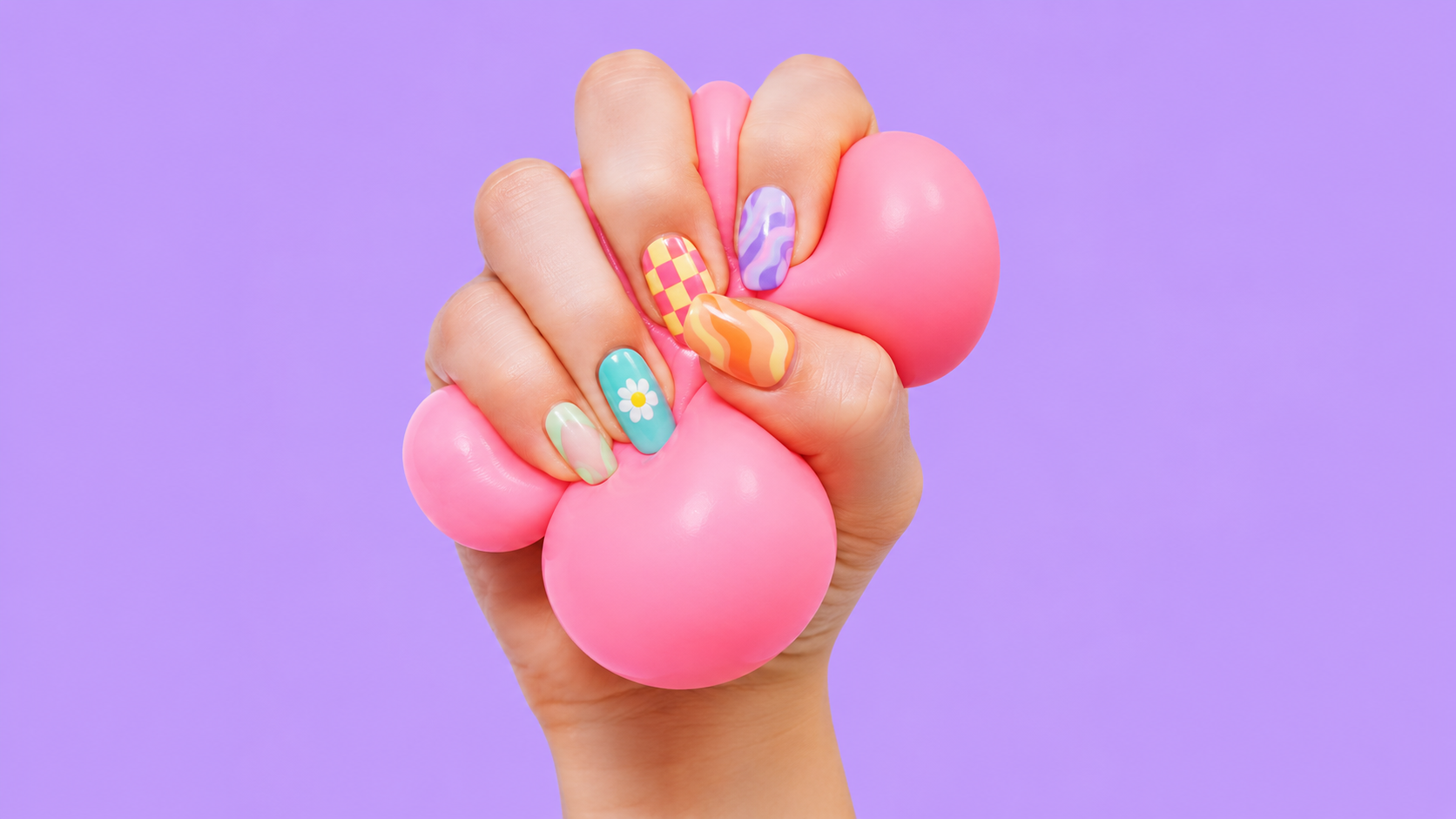 Hand with colorful rainbow and pastel nail art squeezing pink slime on a purple background.