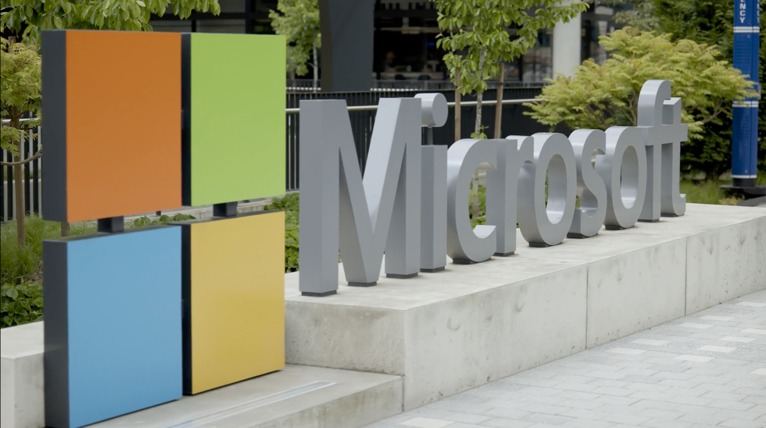 Outside Microsoft building with large white 'Microsoft' sign and colorful geometric sculptures, green trees, and modern architecture in the background.