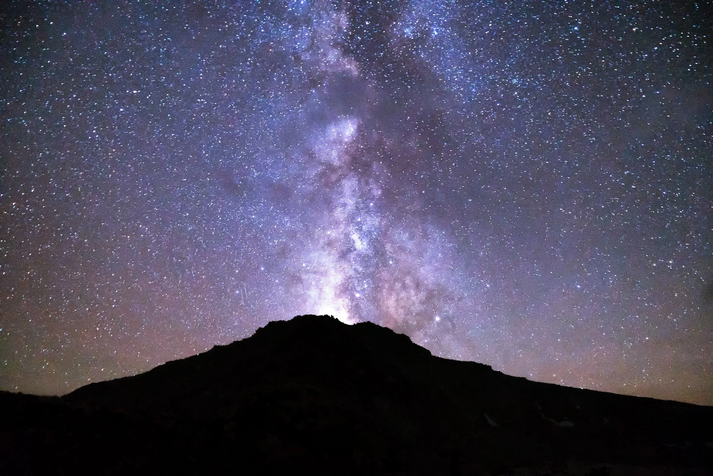 Night sky filled with stars and the Milky Way galaxy above a silhouette of a mountain.