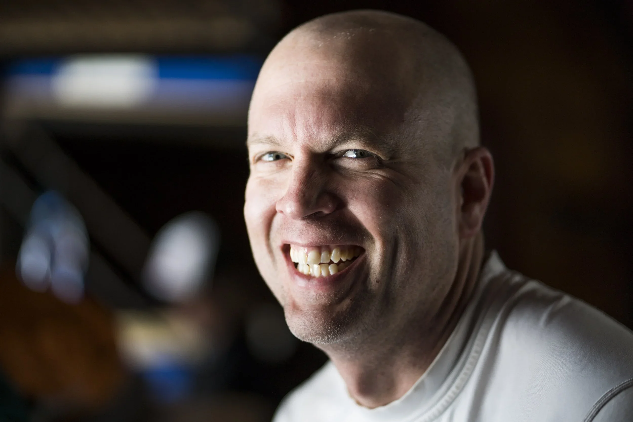 A smiling man with a shaved head, showing his teeth.