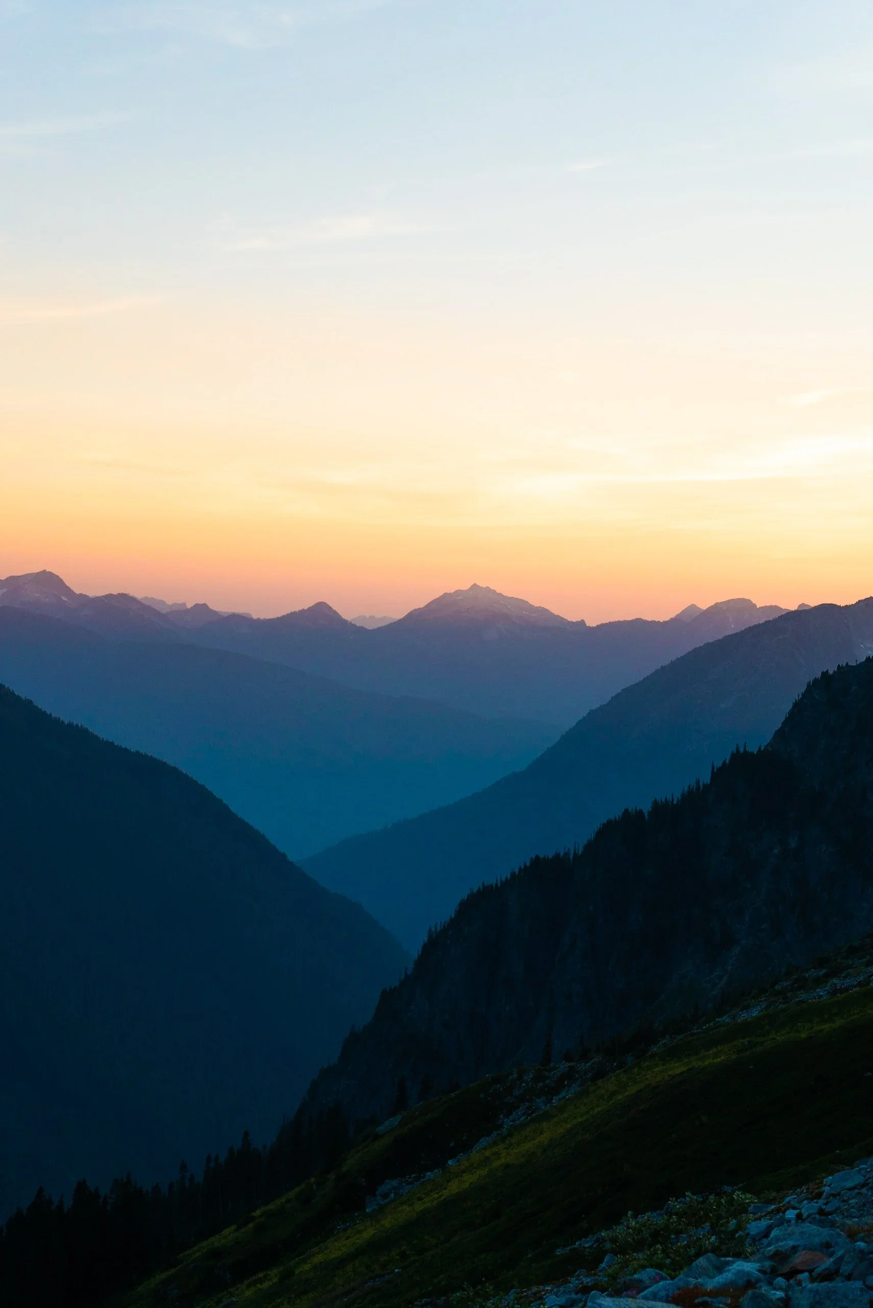 A mountain range at sunset with a colorful sky, some clouds, and distant peaks.