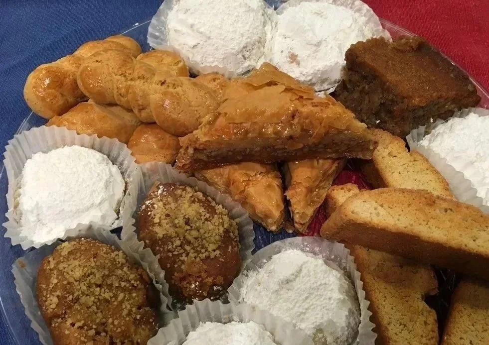 Assorted Greek desserts including kouroumbiedes, melomakarona, koulourakia, paximadia, and karidopita arranged on a platter.