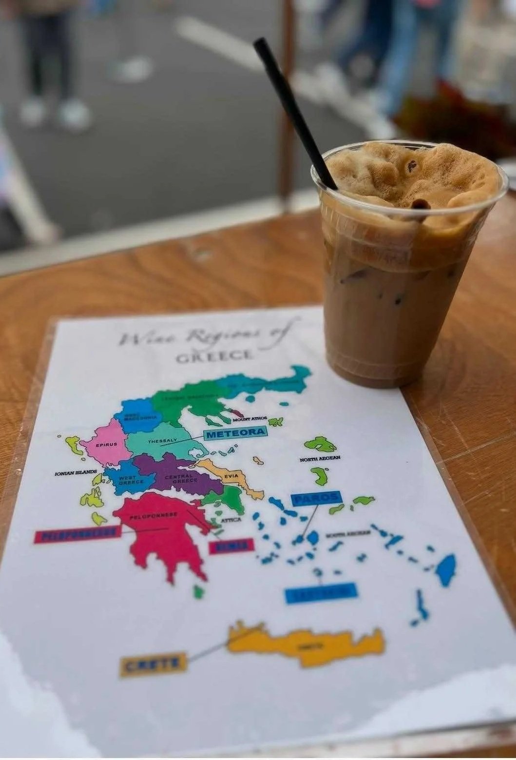 A Greek frappe sits on a table on top of a colorful map of the wine regions in Greece