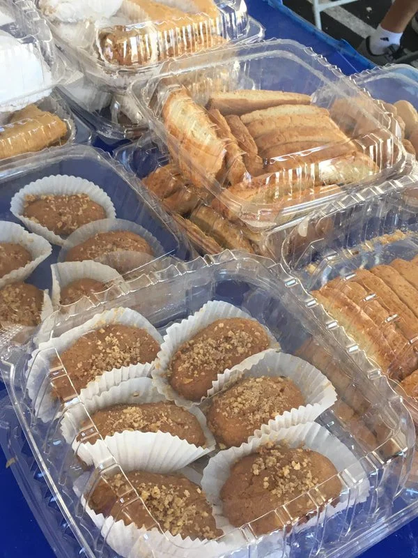 Assorted Greek baked goods in clear plastic containers, including melomakarona, paximadia, and koulourakia.