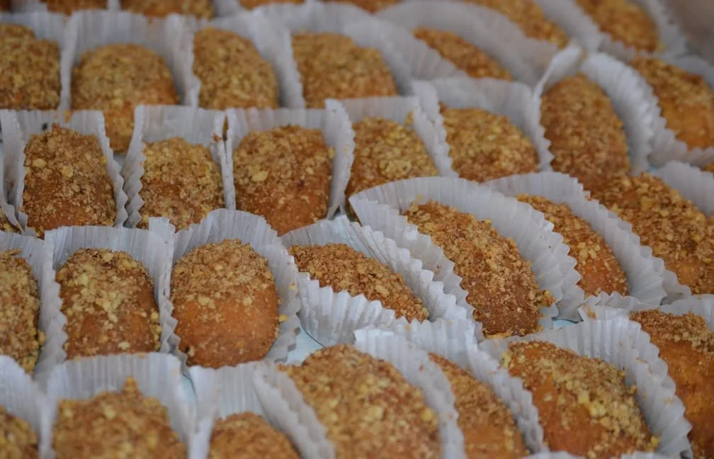 rows of Greek melomakarona cookies topped with honey and chopped walnuts in white paper liners