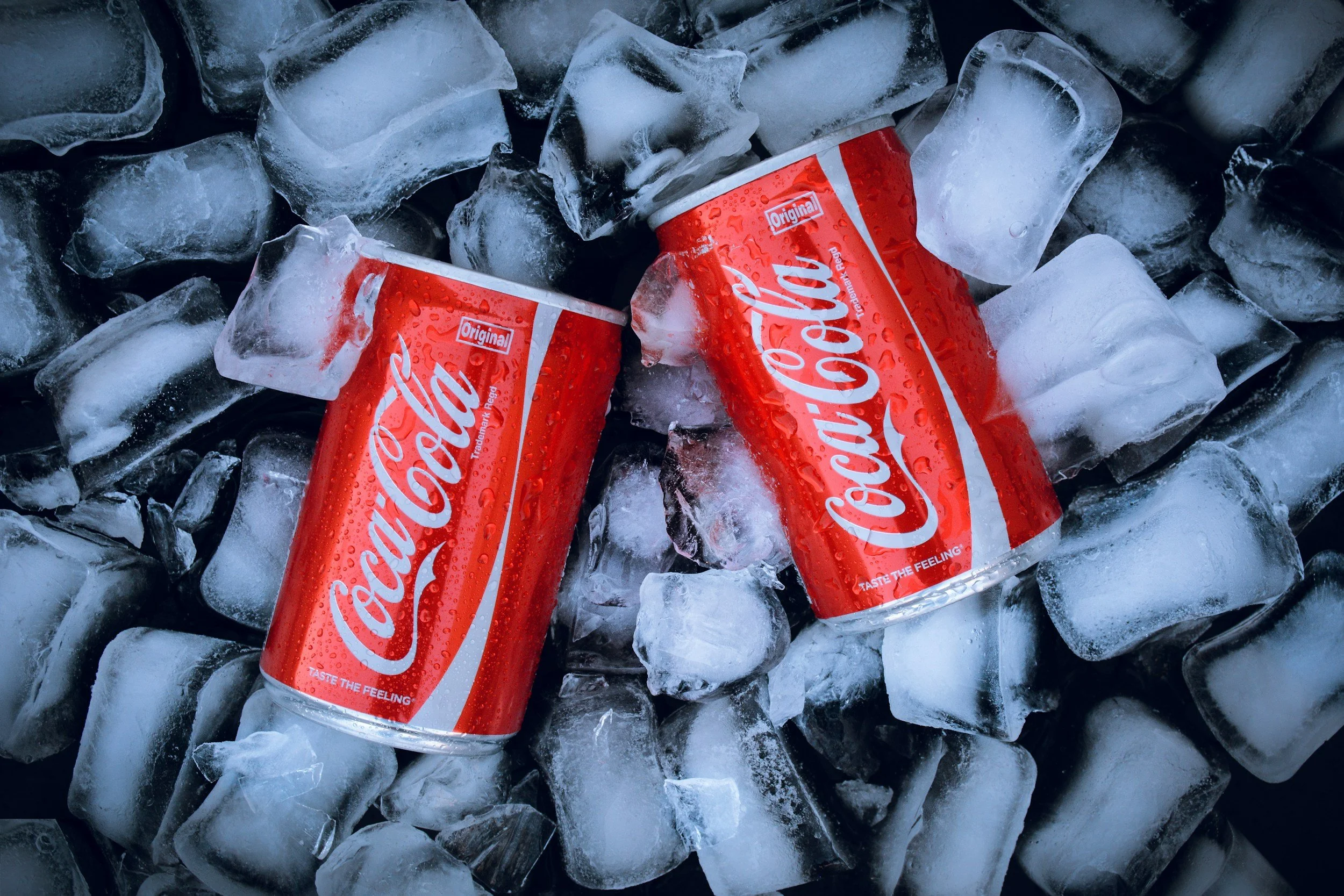 Two red cans of Coca-Cola soda lying on top of ice cubes.