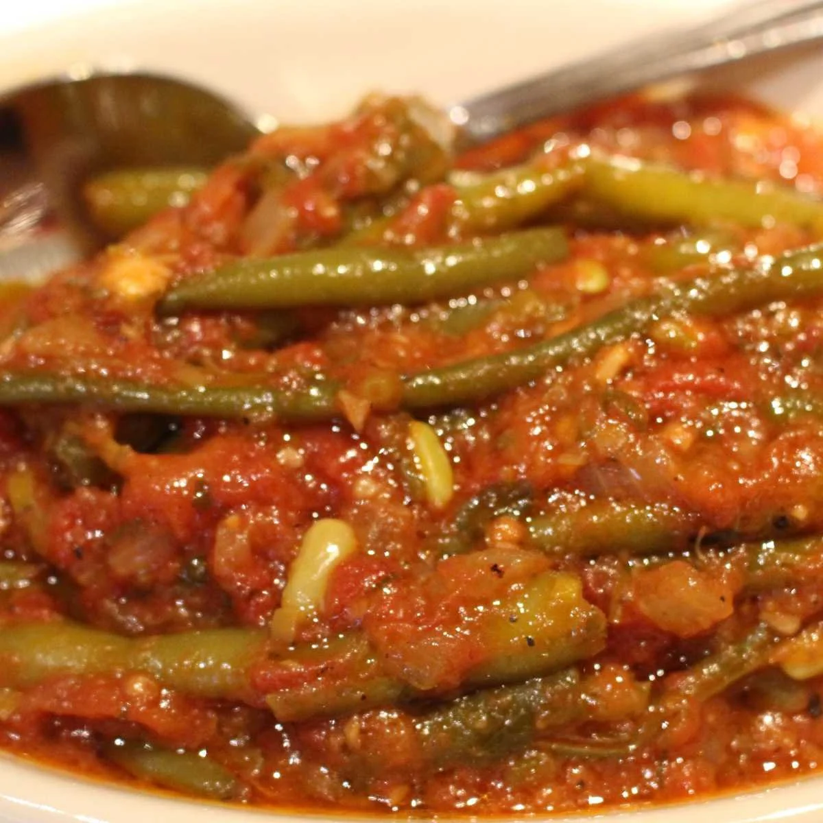 Close-up of a plate of fasolakia, green beans cooked in tomato sauce with herbs and spices.