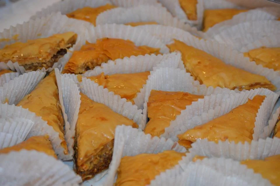 Several triangle pieces of baklava in white paper cups, arranged in a tray.