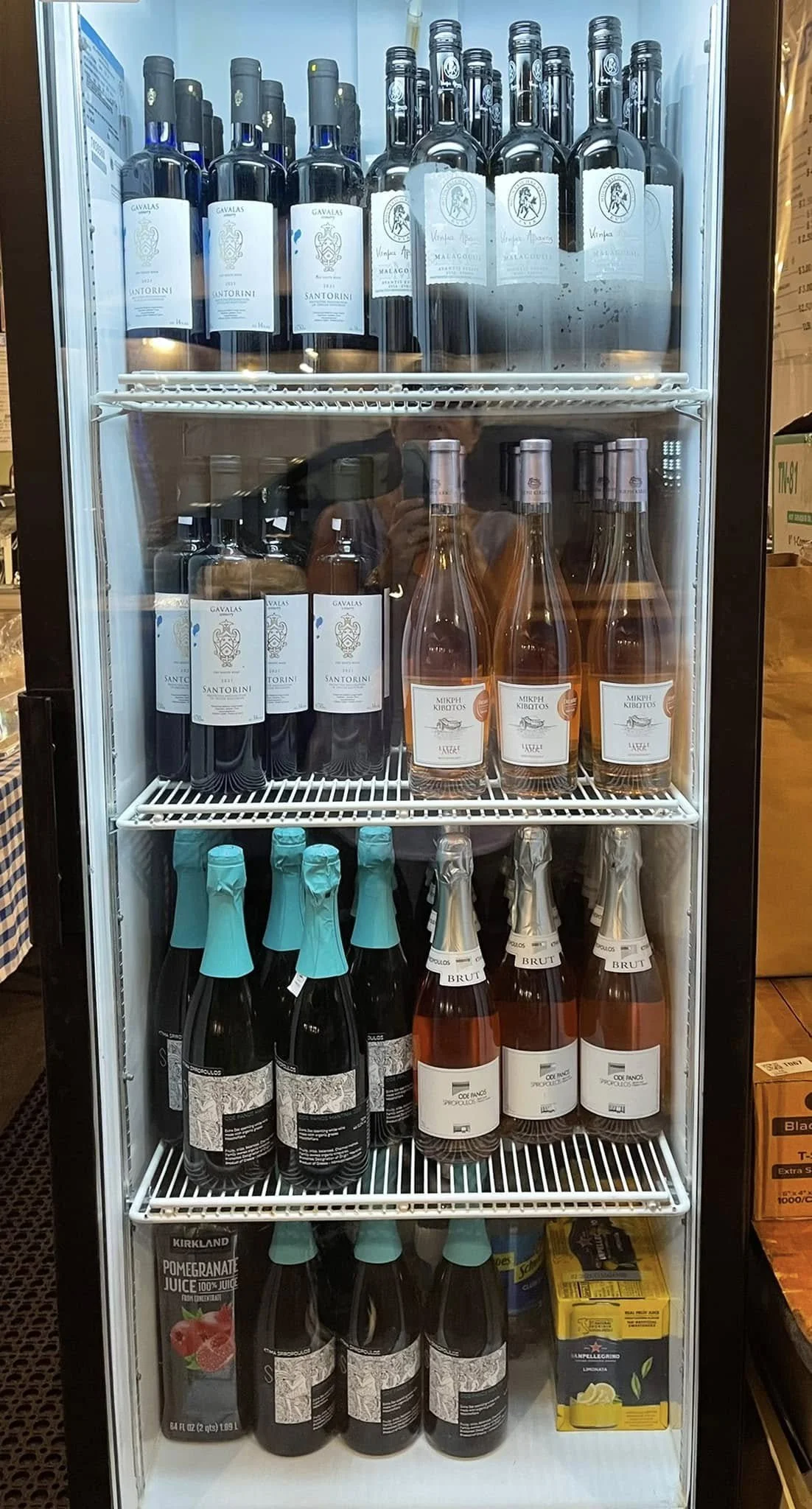A refrigerator with multiple bottles of Greek wine, sparkling wine, and cocktail ingredients inside.