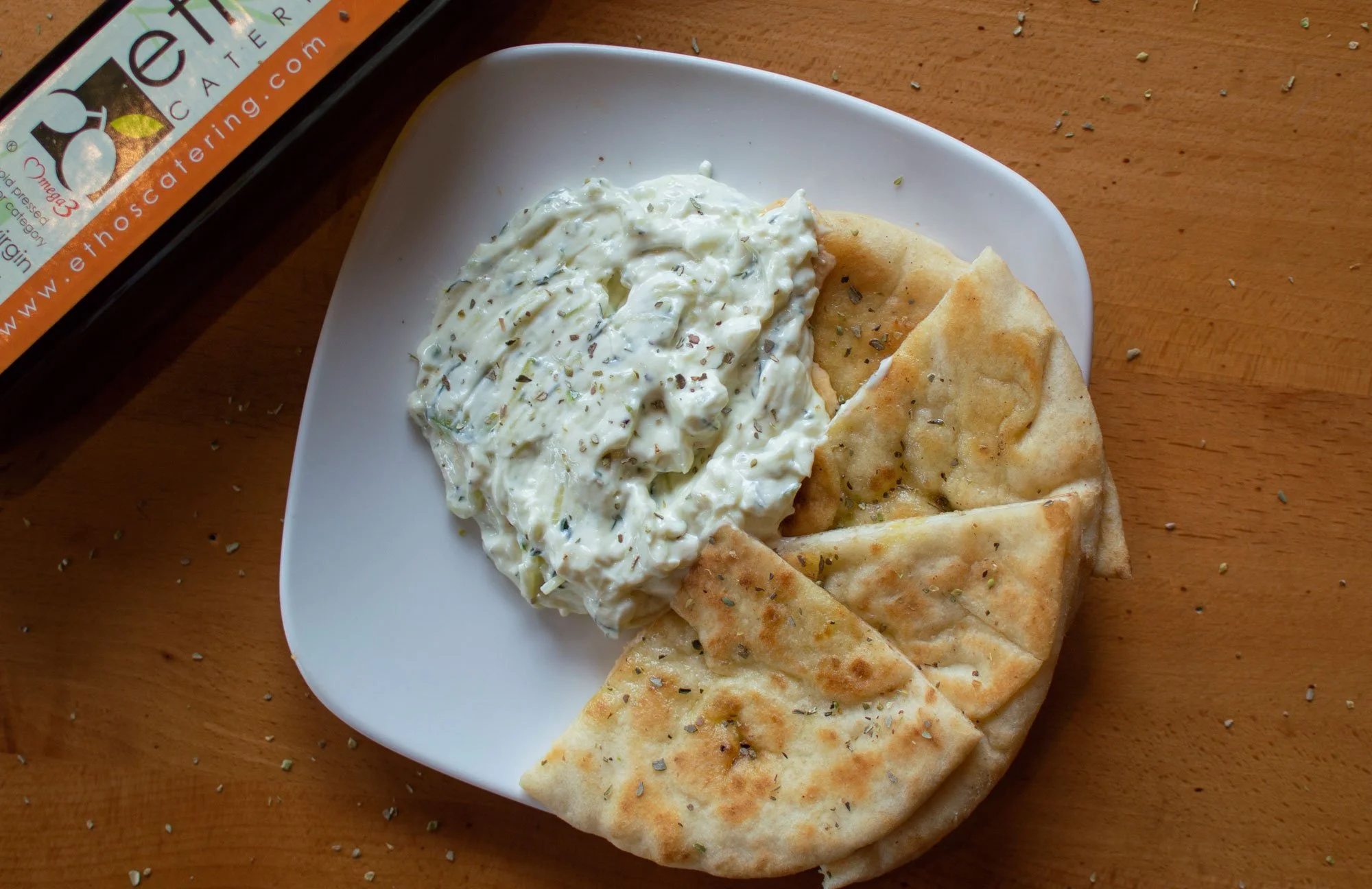 A white plate with pita bread and a bowl of Greek tzatziki dip on a wooden surface