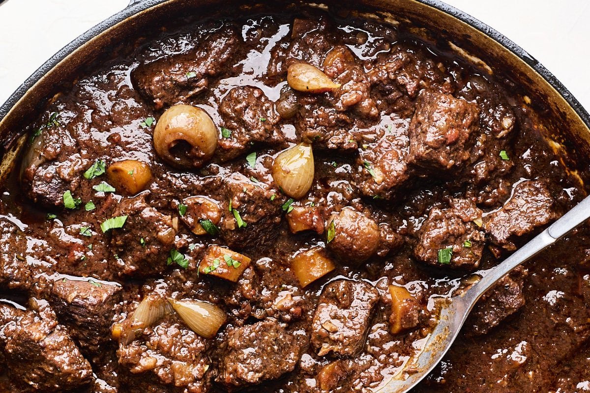 A closeup of stefado, a Greek stew with chunks of beef, carrots, potatoes, and pearl onions.