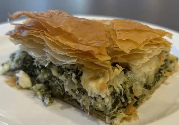 A slice of spanakopita, Greek spinach and cheese pie topped with flaky phyllo dough.